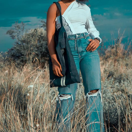 Person wearing ripped jeans and a white shirt standing in a natural setting with water in the background