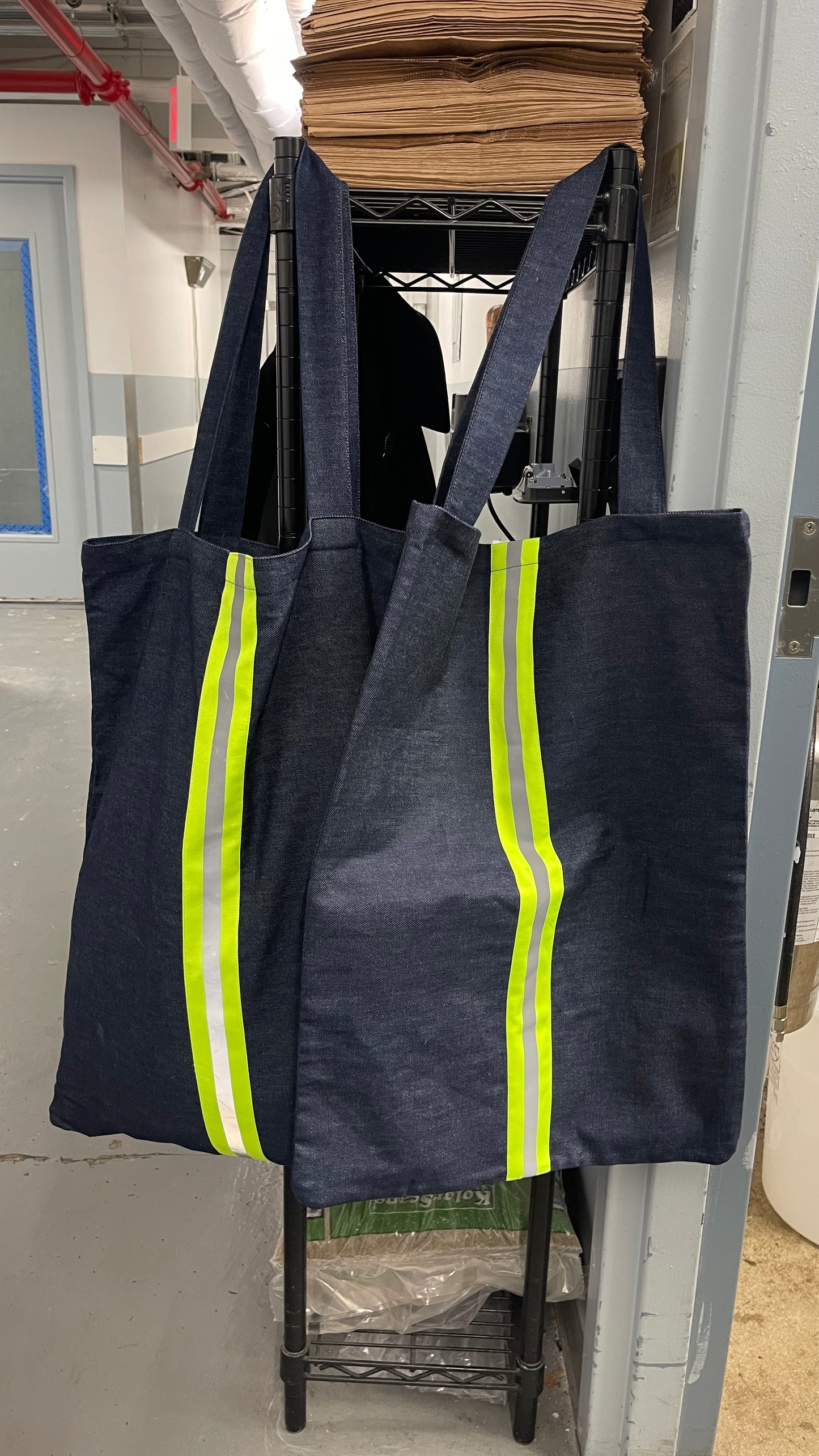 Two dark blue tote bags with reflective yellow stripes hanging on a rack.