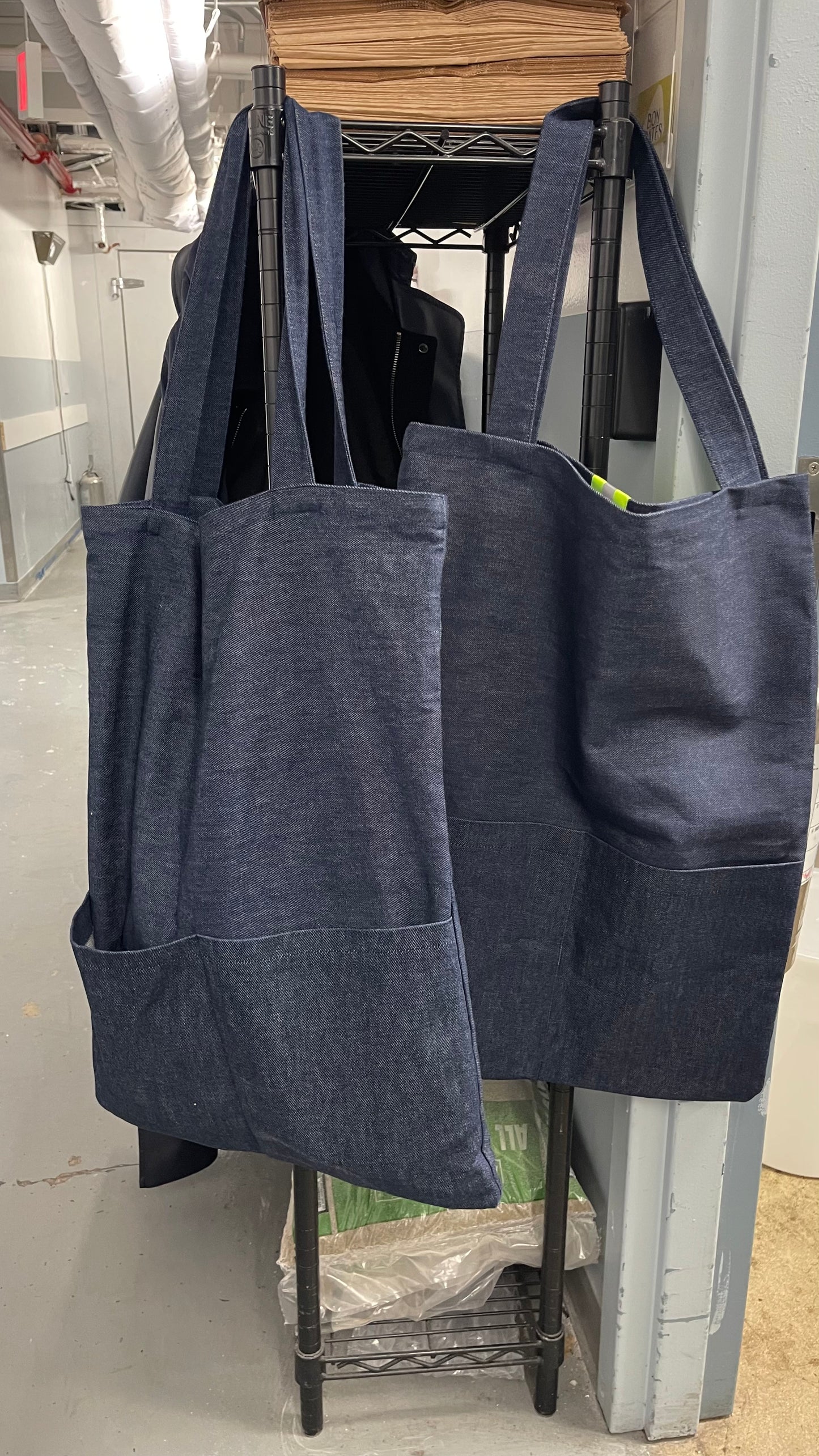 Two dark blue tote bags hanging on a rack in an indoor setting.